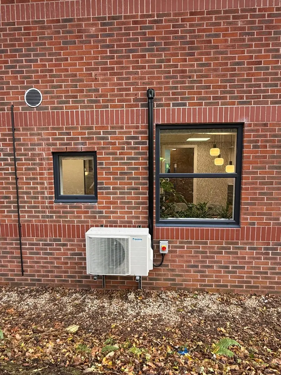 Daikin outdoor unit mounted low on a brick wall beneath a window