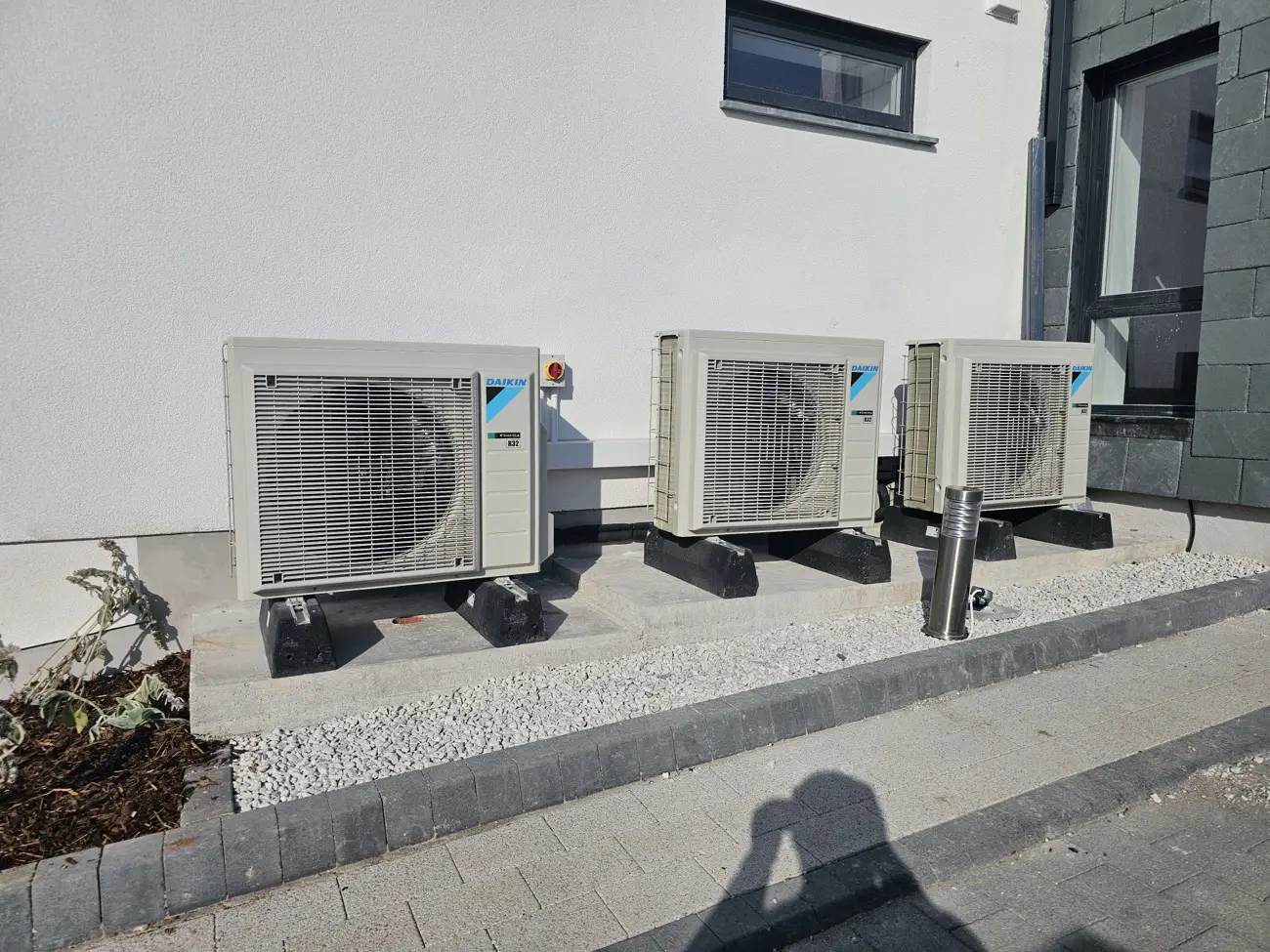 Three Daikin air conditioning outdoor units installed on mounting blocks beside a house