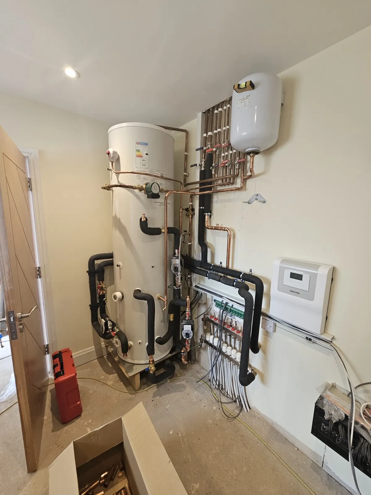 Heat pump plant room with hot water cylinder, insulated pipework and underfloor heating manifold